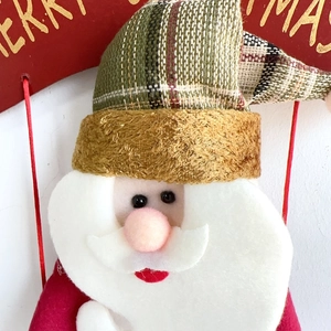 Detail der Weihnachtsmann-Plüschfigur mit Filzbart und goldener Merry Christmas Tafel
