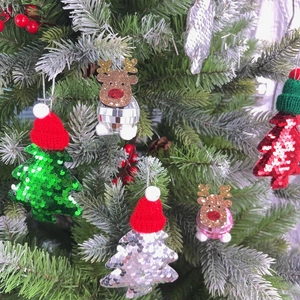 Close-up of sequin Christmas tree and disco ball reindeer ornaments on snowy branches