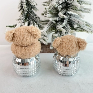 Plush brown bear heads with reflective disco ball bases on winter snowy pine background