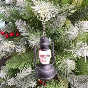 Close-up of a glowing skull lantern keychain with pink LED light hanging on a tree branch