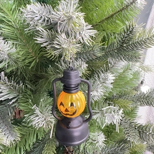 Hanging Halloween pumpkin lantern ornament with Jack-o'-lantern face on pine branch