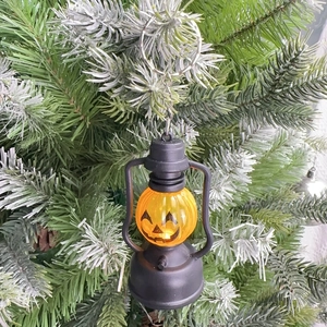 Close-up of orange pumpkin lantern ornament hanging on a green tree branch