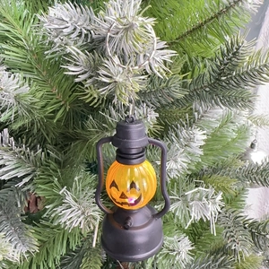 Close-up of Halloween pumpkin lantern keychain hanging on green pine tree branches
