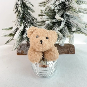Plush brown teddy bear sitting on a silver mirror disco ball festive decoration