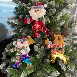 Close-up of sequined Santa, snowman and elk ornaments hanging on a snowy Christmas tree