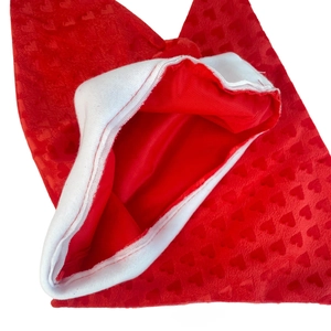 Detail view of red plush Christmas hat featuring embossed heart patterns and white faux fur trim
