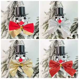 Close-up of four snowman disco ball ornaments with glitter bows on a snowy pine branch