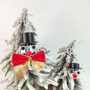 Detailed view of mirror disco ball snowman ornaments with red bow on snowy Xmas tree