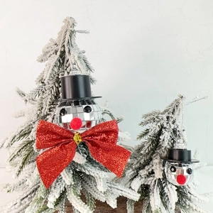 Detail of mirror disco ball snowman ornaments with red bows on snowy Christmas trees
