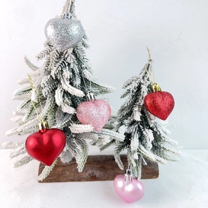 Detail of heart shaped Christmas ornaments in glitter and matte finish hanging on snowed trees