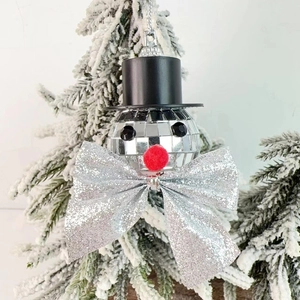 Macro detail of disco ball snowman ornament with silver bow on a Christmas tree branch