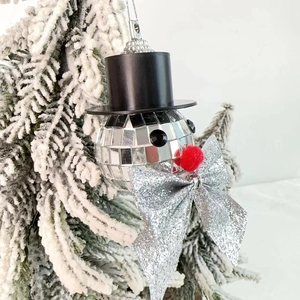 Close-up of disco ball snowman ornament with silver sequins on a snowy Christmas tree branch