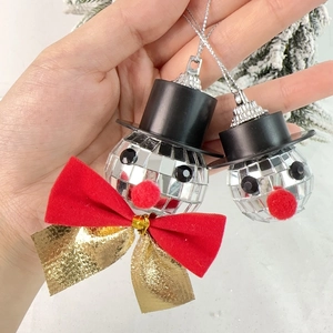 Disco ball snowman Christmas ornament with top hat and red bow on a pine branch