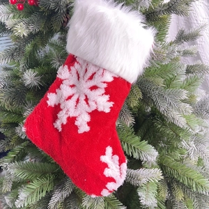 Red plush Christmas stocking with white snowflake pattern hanging on a Christmas tree