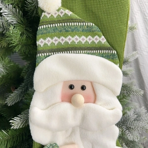 Detail of green knit Christmas stocking featuring a 3D plush Santa Claus on a tree branch