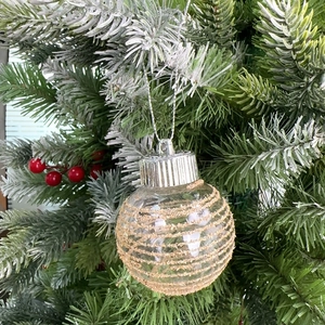 Dettaglio di una palla di Natale avvolta in corda dorata appesa a un ramo di pino innevato