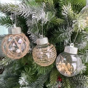 Tre palline di Natale trasparenti con corda di canapa e fiori secchi su albero innevato