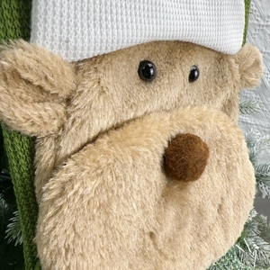 Close-up of green knitted Christmas stocking featuring a 3D plush bear and white cuff