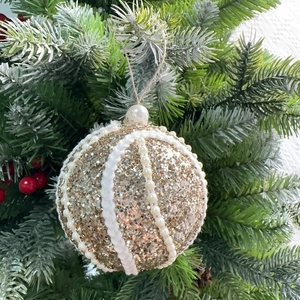 Detail of 8cm gold Christmas ball with white pearls and glitter on green tree branches
