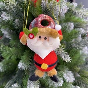 Close-up of Santa Claus plush pendant with a red hat hanging on a frosted Christmas tree