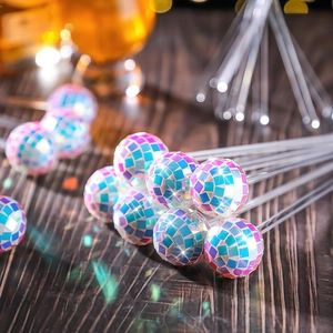 Close-up of disco mirror ball cocktail stirrers on a wooden table with party lighting