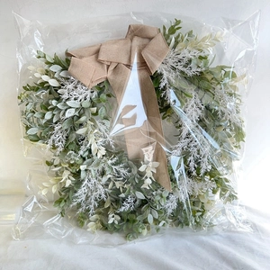 Close-up of artificial greenery wreath with a large brown burlap bow in protective packaging