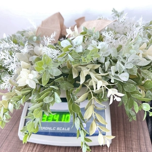 Close-up of artificial plant wreath with linen bow showing a weight of 334g on a scale