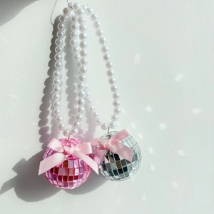 Détail de boules disco rose et argent avec perles blanches et nœuds en soie au mur