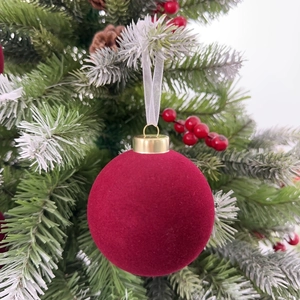 Detailed view of dark red flocked Christmas ball ornament hanging on a snowy pine branch