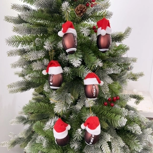Close-up of American football ornaments with Santa hats on snowy Christmas tree branches