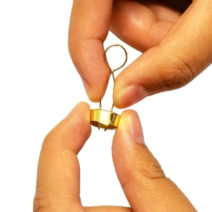 Hand holding golden metal Christmas ornament cap with flexible spring wire mechanism