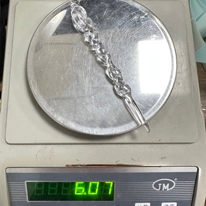 Macro detail of a 6.07g clear acrylic icicle ornament being weighed on a digital scale