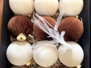 Detail of plush velvet Christmas balls in cream and brown with gold caps in a gift box