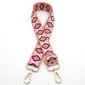 Detail of adjustable woven bag strap with pink geometric diamond patterns and gold hooks