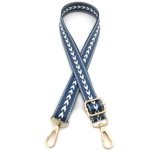Detail of adjustable canvas bag strap with white arrow pattern and golden metal buckles