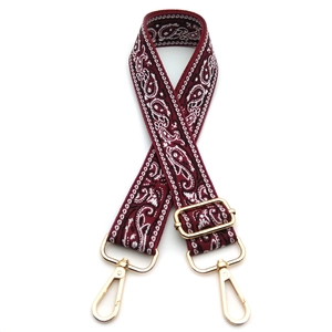 Detail view of ethnic paisley burgundy woven shoulder strap with gold metal hooks and buckle