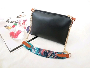 Detail of black crossbody bag featuring a blue paisley printed strap and gold chain link