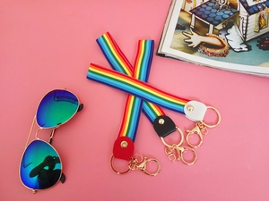 Detail of rainbow striped wristlet straps with gold lobster clasps on pink background