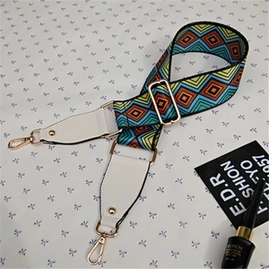 Detail of colorful geometric woven bag strap with white leather ends and gold hooks