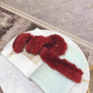 Close-up of deep red faux fur bag strap with gold metal hooks on a marble table