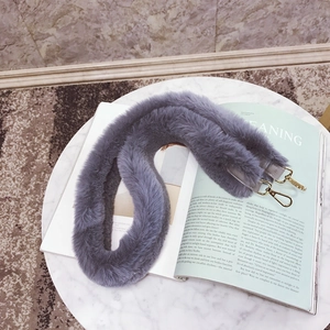 Detail view of a gray faux fur shoulder strap with gold metal lobster clasps on a magazine