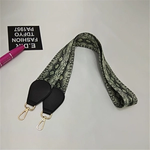 Detail view of snakeskin print bag strap with golden metal carabiners and leather ends