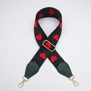 Detail view of the embroidered red heart pattern on the black wide woven bag strap