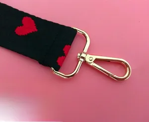 Detail of black woven strap with red heart embroidery and golden metal swivel hook