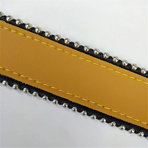 Close-up of yellow and black leather bag strap with silver metal bead trim and stitching