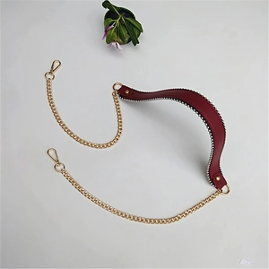 Macro shot of gold metal bag chain with burgundy leather shoulder strap and lobster clasps