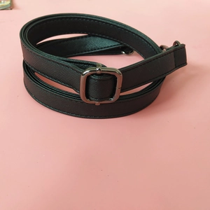 Detail of black cross-grain leather bag strap with gunmetal buckle on pink background