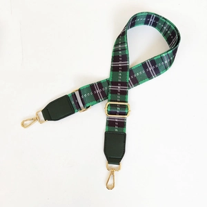 Detail view of green plaid canvas bag strap with leather ends and golden metal snap hooks