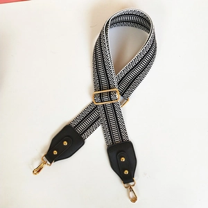 Detail of adjustable black and white geometric woven strap with golden metal hardware