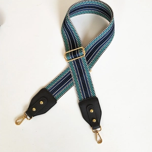Detail showing geometric woven wide strap with gold snap hooks and black leather ends
